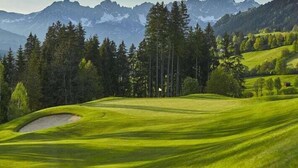 A golf course with a flagstick, surrounded by trees and mountains. - Chalet Belle Kitz 1 by belle-stay (Kitzbühel)