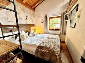 Una habitación con una cama litera, un escritorio de madera, una ventana con cortinas y un cuadro colgado en la pared.