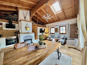 Interior acogedor de una cabaña con una mesa de comedor de madera, una chimenea, un sofá y un televisor montado en la pared.