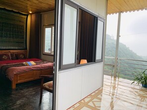 Relax in a spacious room with a large bed, wooden headboard, and a view of lush green surroundings.