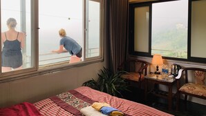 A hotel room with a large bed, a desk with a lamp, and a view of a balcony. - Sapa Dao Homestay (Sa Pa)