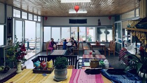 A spacious room with wooden ceilings and large windows, featuring a dining area with tables and chairs, a kitchen area with hanging plants, and a view of the outside. - Sapa Dao Homestay (Sa Pa)