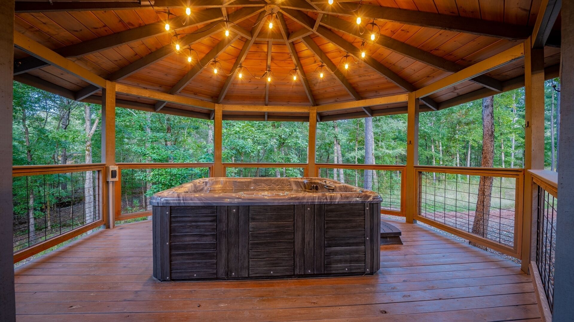 A hot tub in a wooden gazebo with a view of a forest.