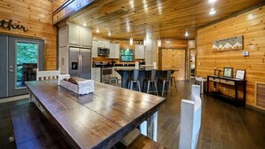 Un'ampia cucina con elettrodomestici moderni, una zona pranzo con un grande tavolo in legno e un angolo bar con sgabelli.