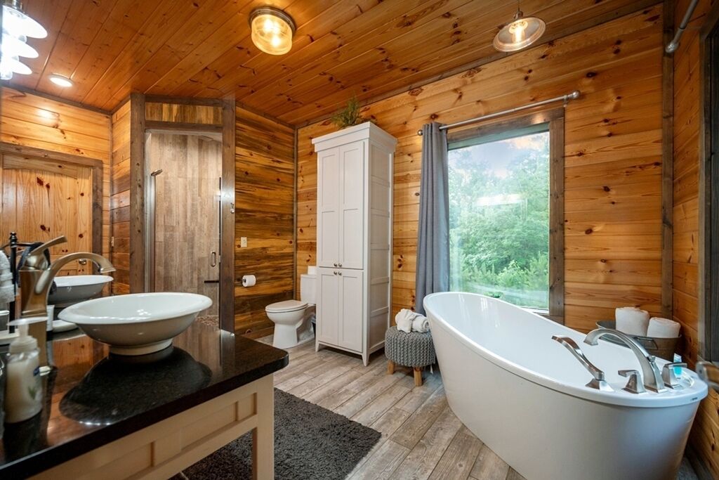 A wooden cabin bathroom with a freestanding bathtub, two sinks, a toilet, and a cabinet.