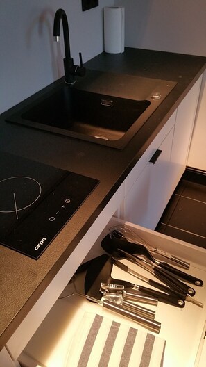 Una cocina con encimera negra, un lavabo y un cajón con utensilios de cocina.