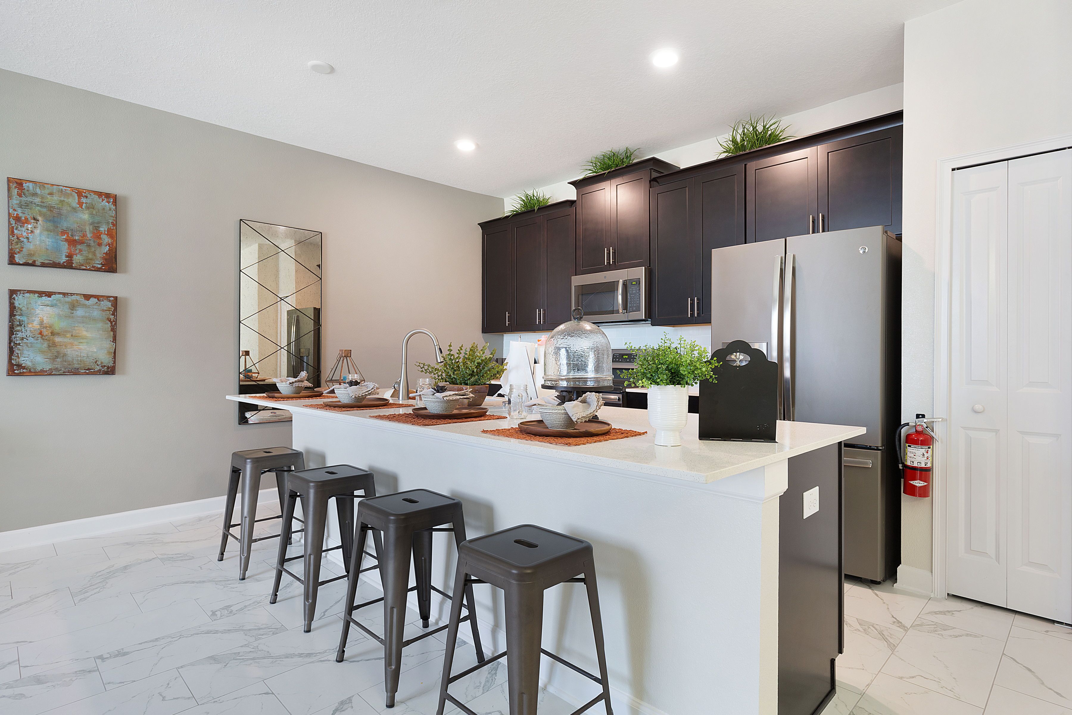 A modern kitchen with dark cabinets, a white island with bar stools, stainless steel appliances, and decorative plants.