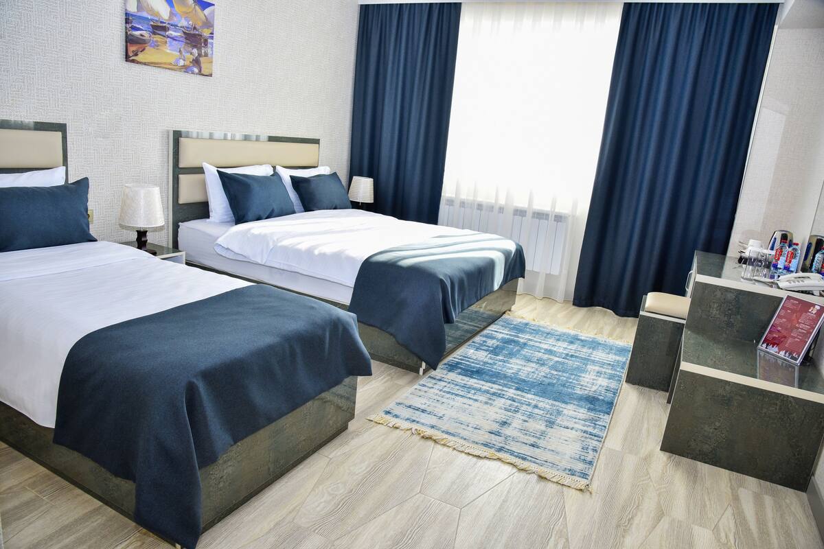 Une chambre d’hôtel avec deux lits, un bureau, une chaise et une grande fenêtre avec des rideaux.