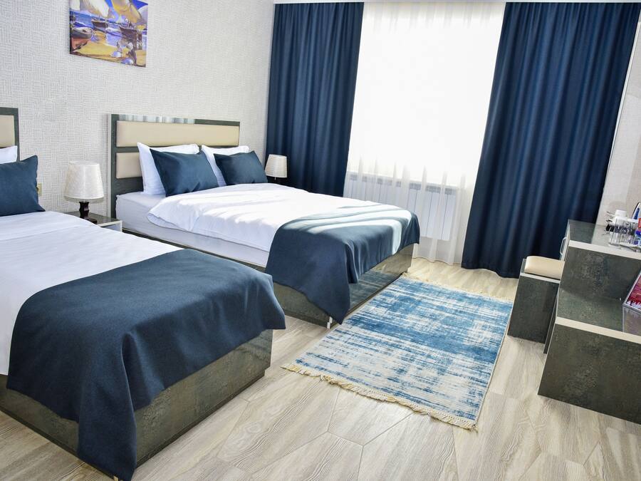 A hotel room with two beds, a desk, a chair, and a large window with curtains.