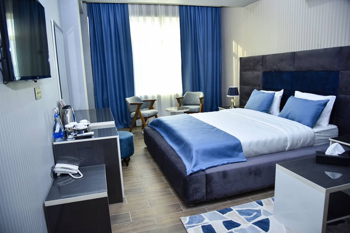 Une chambre d’hôtel moderne dotée d’un grand lit, d’un bureau avec un téléphone, d’une chaise, d’une petite table et d’un téléviseur fixé au mur.