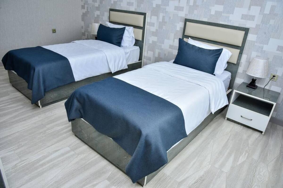Deux lits jumeaux avec des têtes de lit et des pieds de lit assortis, une table de chevet avec une lampe, et un mur décoré d’un motif.