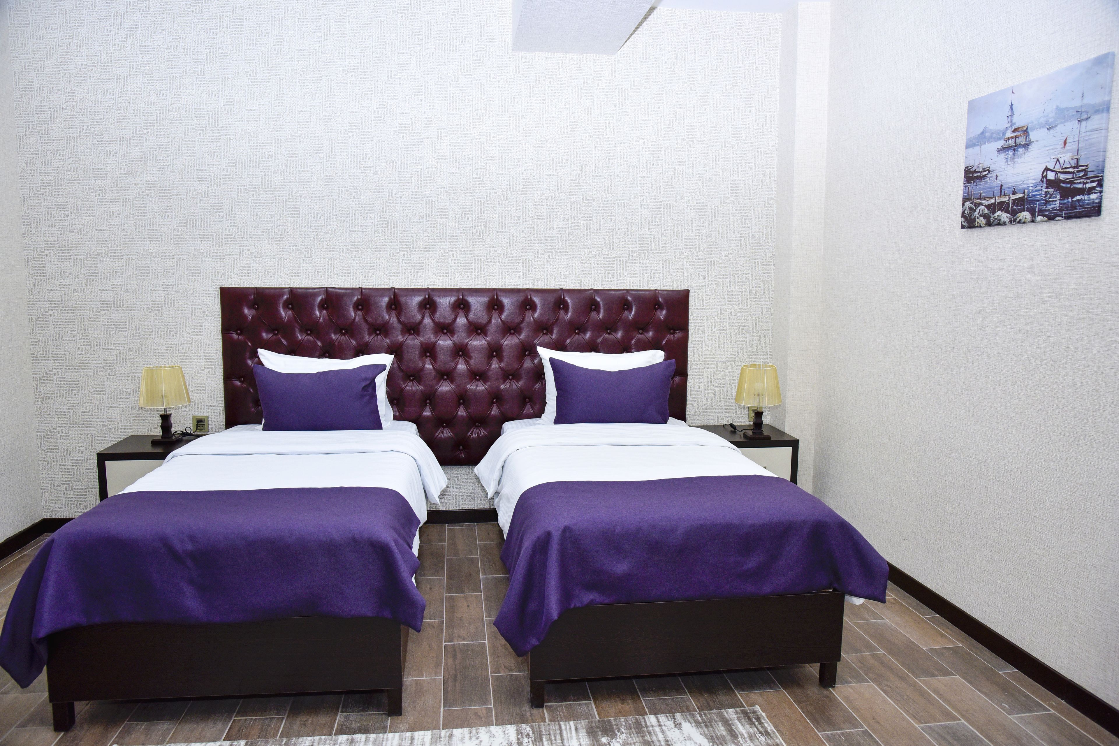 A double bed with a tufted headboard, two bedside tables with lamps, and a painting on the wall.