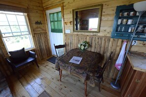 Interior de una cabaña de madera con una mesa de comedor, sillas, un espejo y una estantería con objetos decorativos.