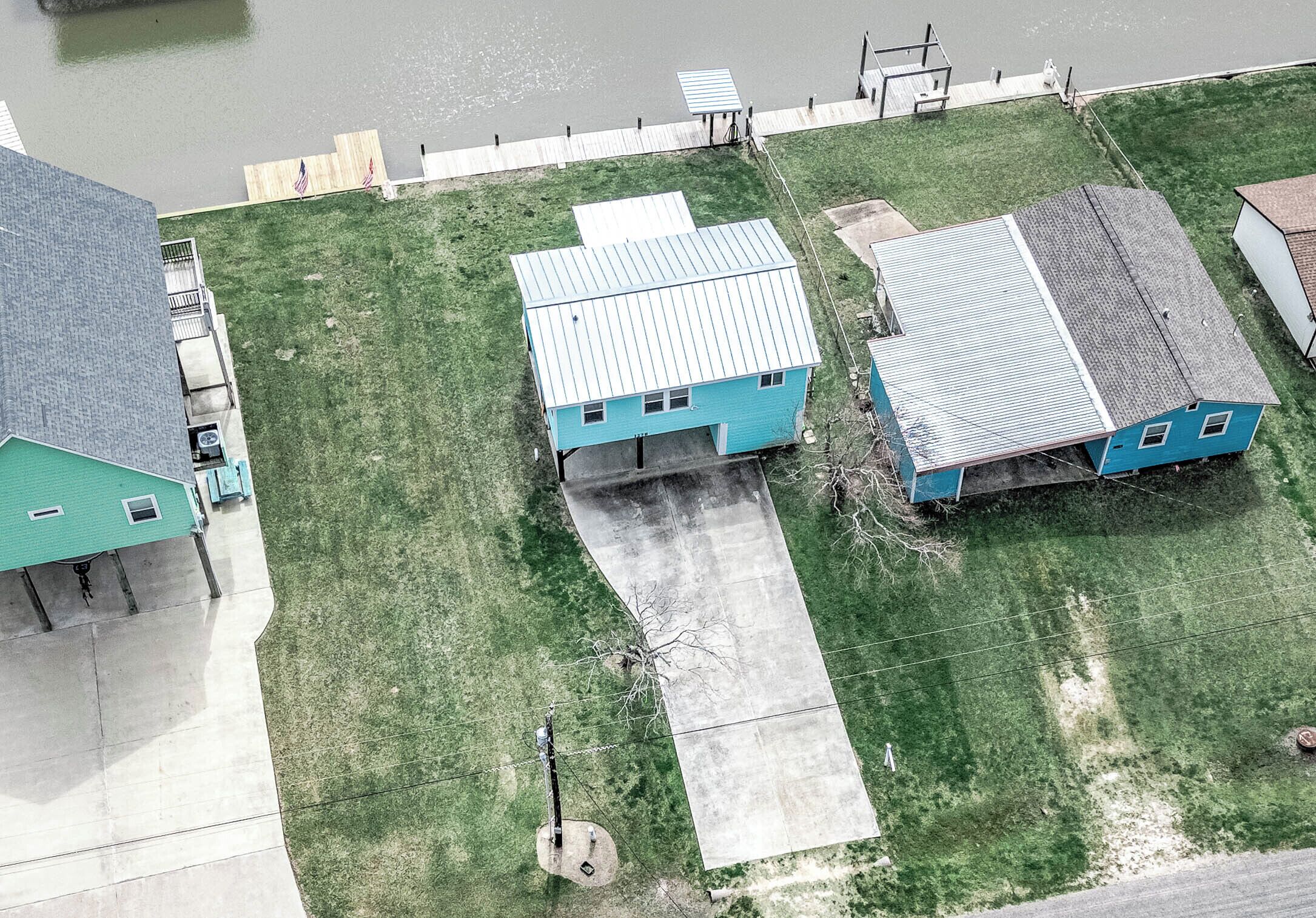 An aerial view of a residential area with three blue houses, a dock, and a grassy lawn.