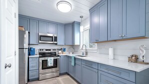 A modern kitchen with blue cabinets, stainless steel appliances, and a white countertop.