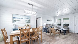 A spacious living area with a wooden dining table and chairs, a sofa set, and a ceiling fan.