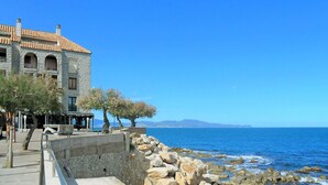 A stone building with a tiled roof by the sea, featuring a stone wall and a paved walkway. - Lovely apartment for 6 people with WIFI and TV (L'escala)