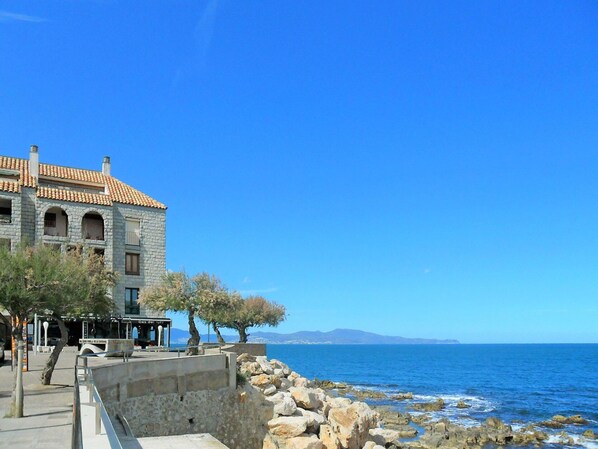 A stone building with a tiled roof near a rocky shoreline.