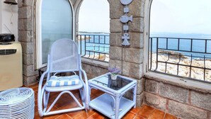 A balcony with a stone wall, a white wicker chair, a small table with a vase, and a view of the sea. - Lovely apartment for 6 people with WIFI and TV (L'escala)