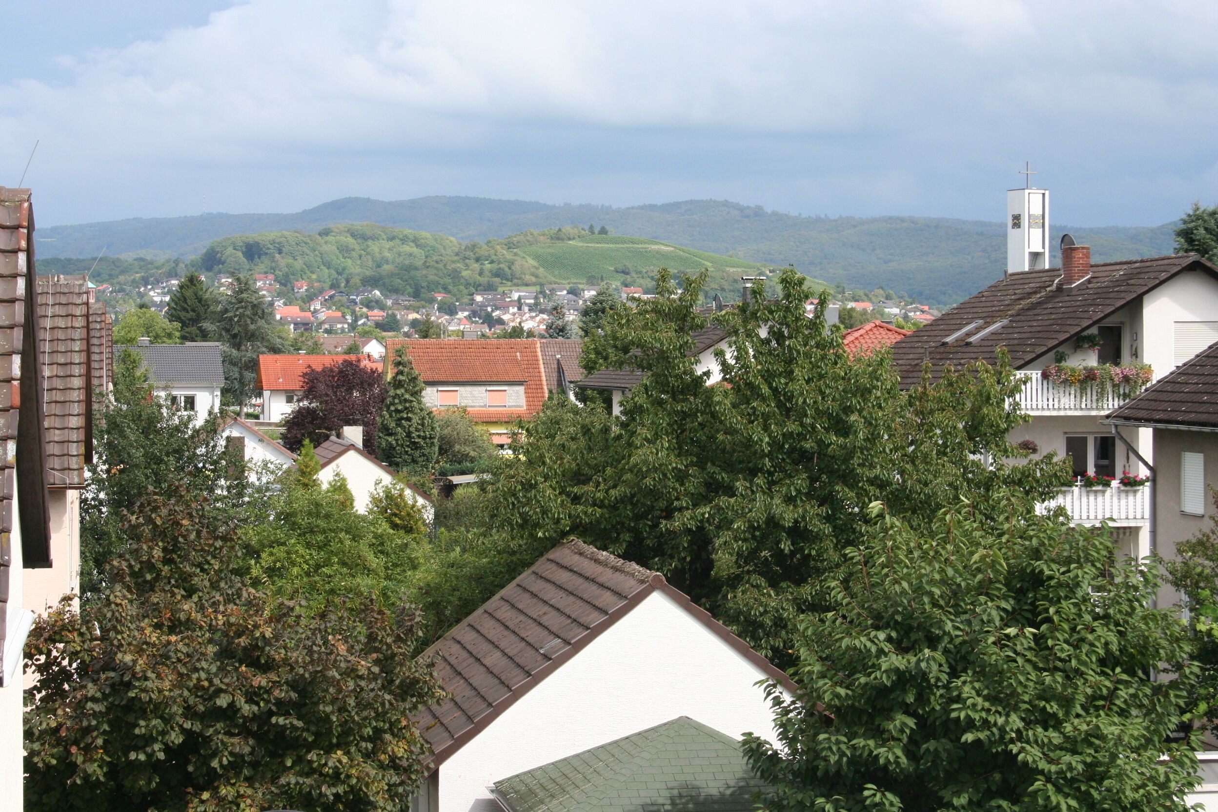 Un quartier résidentiel avec des maisons, des arbres et une vue lointaine sur des collines.