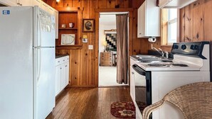 Una cocina compacta con paredes de madera, un refrigerador, una estufa y un lavamanos.