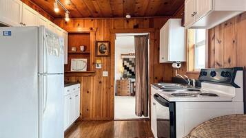 Une cuisine de taille réduite avec des murs en bois, un réfrigérateur, une cuisinière et un évier.