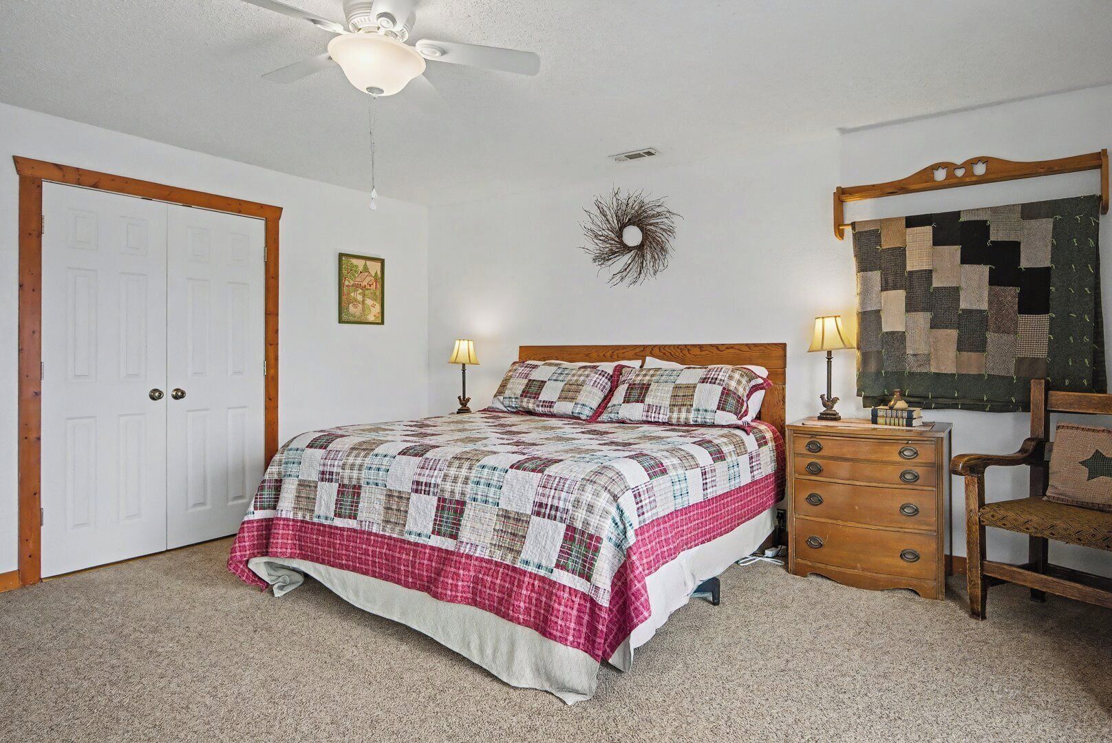 Une chambre à coucher comprenant un lit, des tables de chevet, une chaise, un ventilateur de plafond, une horloge murale et une porte.