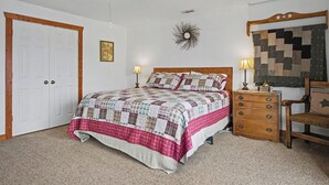Un dormitorio con una cama, mesitas de noche, una silla, ventilador de techo, un reloj de pared y una puerta.