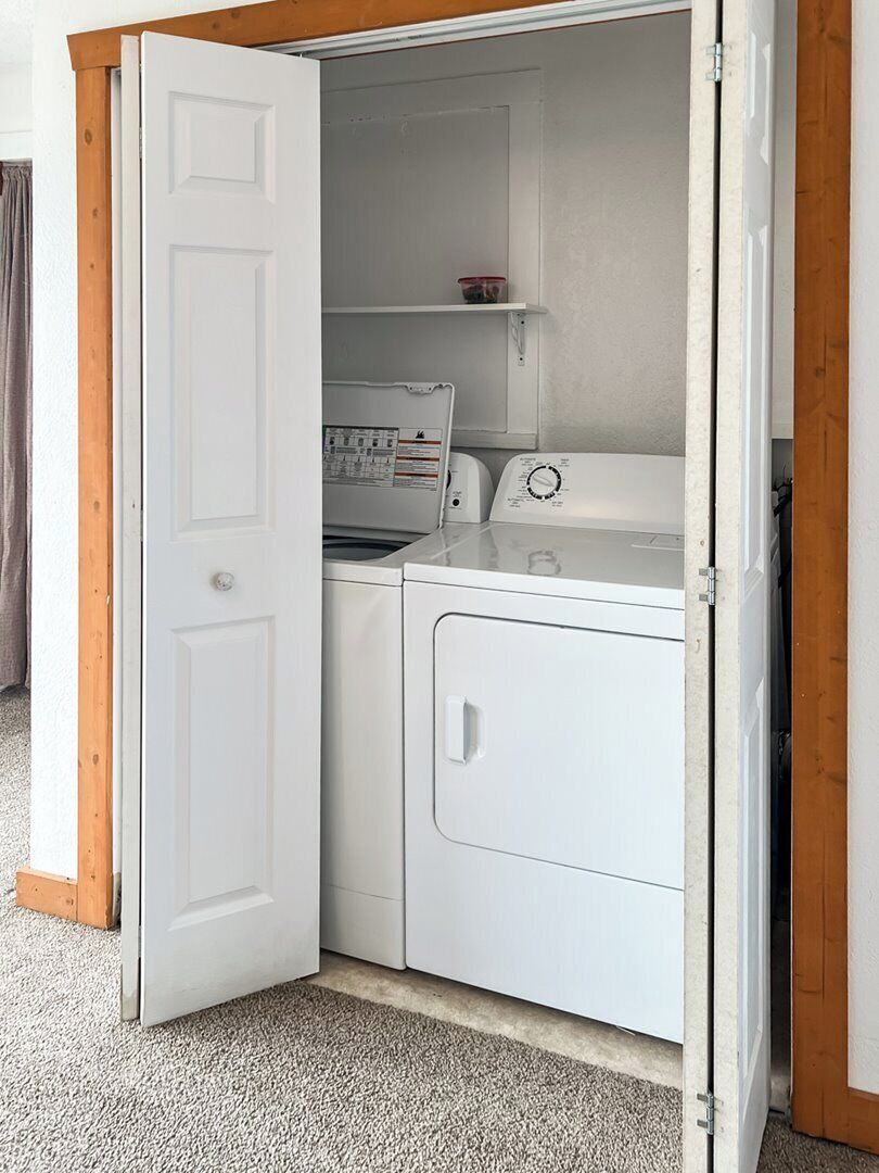 A laundry room with a washing machine, dryer, and a shelf with a container.