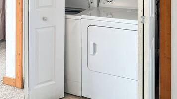 A laundry room with a washing machine, dryer, and a shelf with a container.