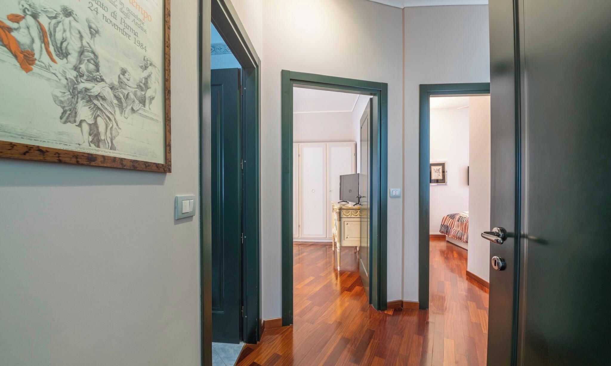 Un couloir doté d’un plancher en bois, une œuvre d’art encadrée accrochée au mur et une porte donnant sur une autre pièce.