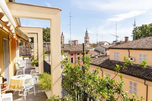A balcony with a table and chairs, overlooking a historic town with traditional buildings and a prominent tower. - Large and bright penthouse in the heart of the city of Parma near the station (Parma)
