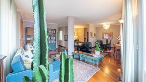 Un salon spacieux avec un grand téléviseur à écran plat, un canapé bleu, une table basse et un cactus.