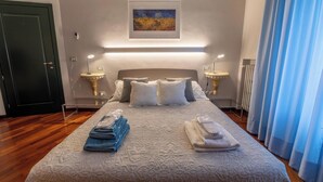 Une chambre d’hôtel avec un lit, deux tables de chevet, un tableau au mur et une fenêtre avec des rideaux.