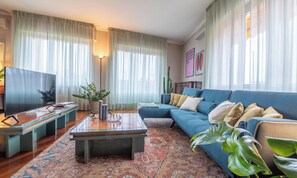Un salon avec un canapé bleu, une table basse, un téléviseur et un tapis à motifs.