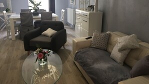 Ein modernes Wohnzimmer mit Sofa, Sessel und einem Glastisch mit Blumen.