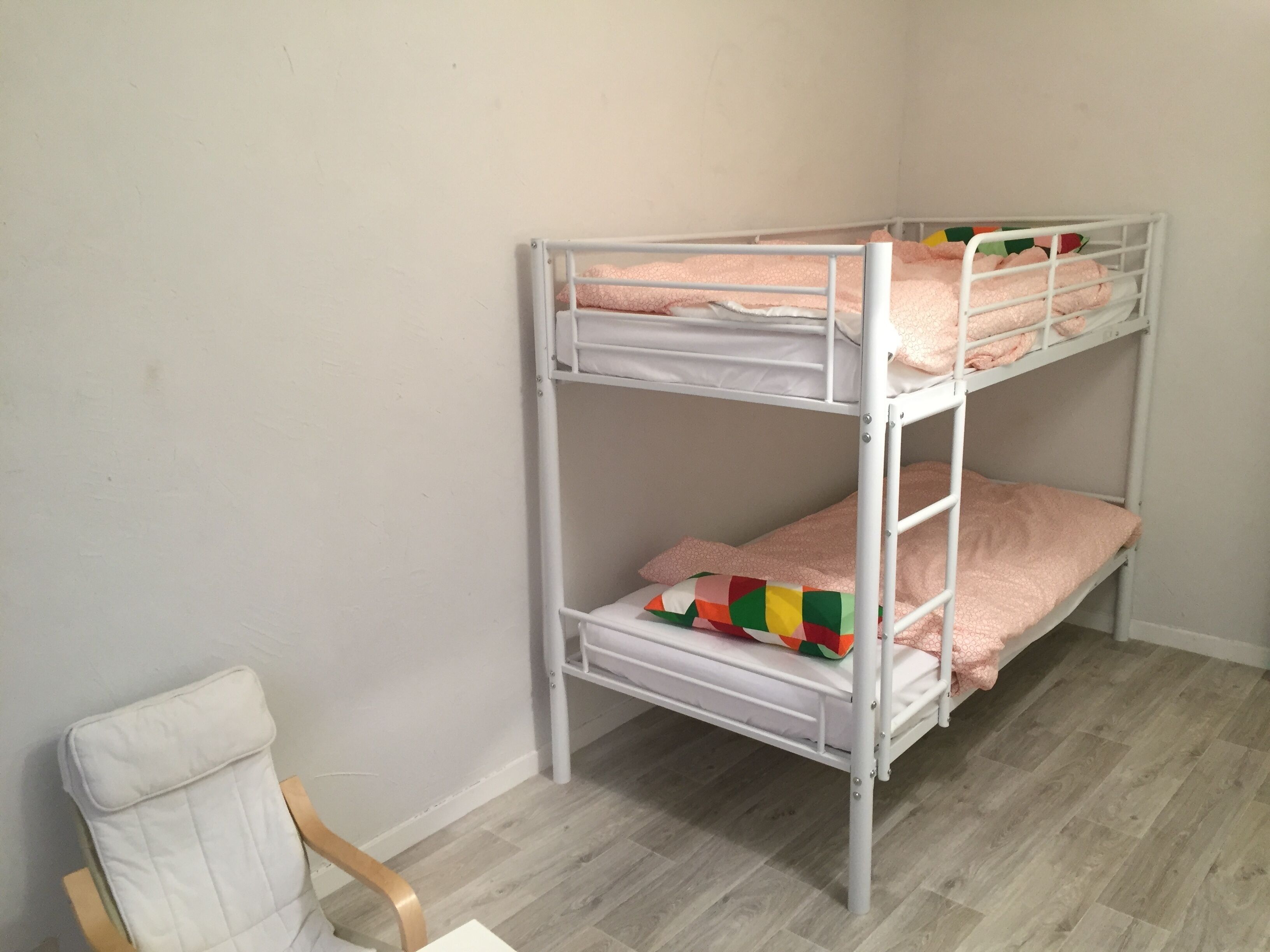 Kerrossänky, jossa on kaksi tasoa, puinen tuoli ja pelkistetty seinä.