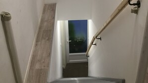 Eine Treppe mit Geländer, ein Ausblick durch ein Fenster und eine Tür am unteren Ende.