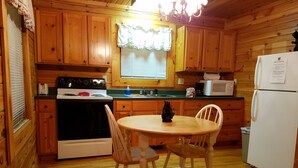 A wooden cabin kitchen with a stove, microwave, refrigerator, and a dining table with chairs.