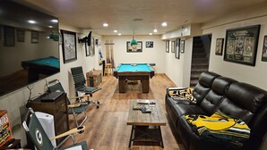 A room with a pool table, a leather couch, a coffee table, and a TV.