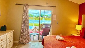 Hotelkamer met een bed, bureau, stoel, dressoir en uitzicht op een zwembad en groen.