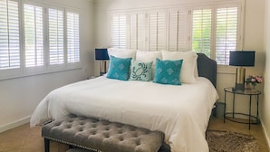 A bedroom with a bed, two bedside tables, a bench, and a ceiling fan. - Walk to the BEACH and close to DOWNTOWN - the perfect location! The Main Suite (Ocean Springs)