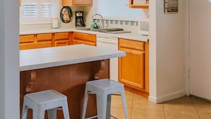 A compact kitchen with wooden cabinets, a white countertop, and two stools. - Walk to the BEACH and close to DOWNTOWN - the perfect location! The Main Suite (Ocean Springs)