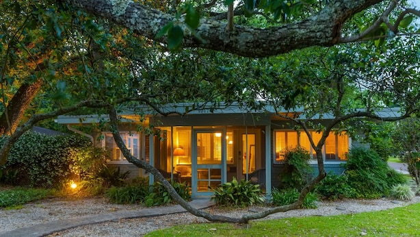 A modern house with a glass facade, surrounded by lush greenery and a gravel pathway. - Walk to the BEACH and close to DOWNTOWN - the perfect location! The Main Suite (Ocean Springs)