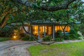 Una casa moderna con fachada de vidrio, rodeada de vegetación exuberante y un camino de grava.
