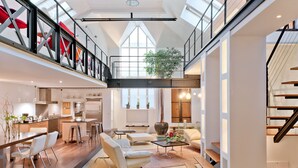 En rymlig interiör i loftstil med en övre våningsplan, ett öppet kök och ett stort fönster som släpper in naturligt ljus.