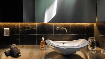 Une salle de bain moderne avec un grand lavabo sur pied, des carreaux foncés et un miroir fixé au mur.