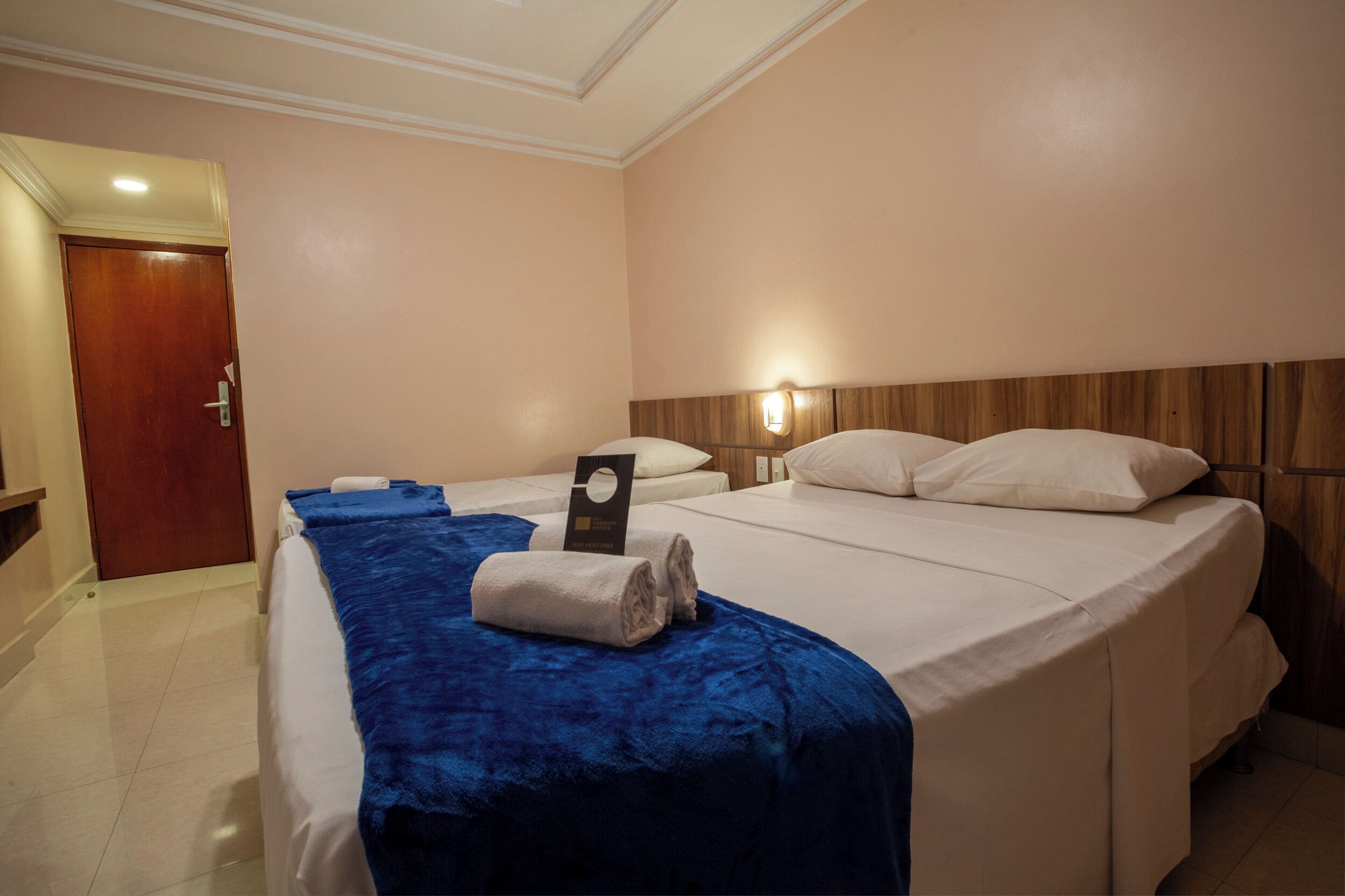 A hotel room with two beds, a wooden headboard, a blue bedspread, and a white door.
