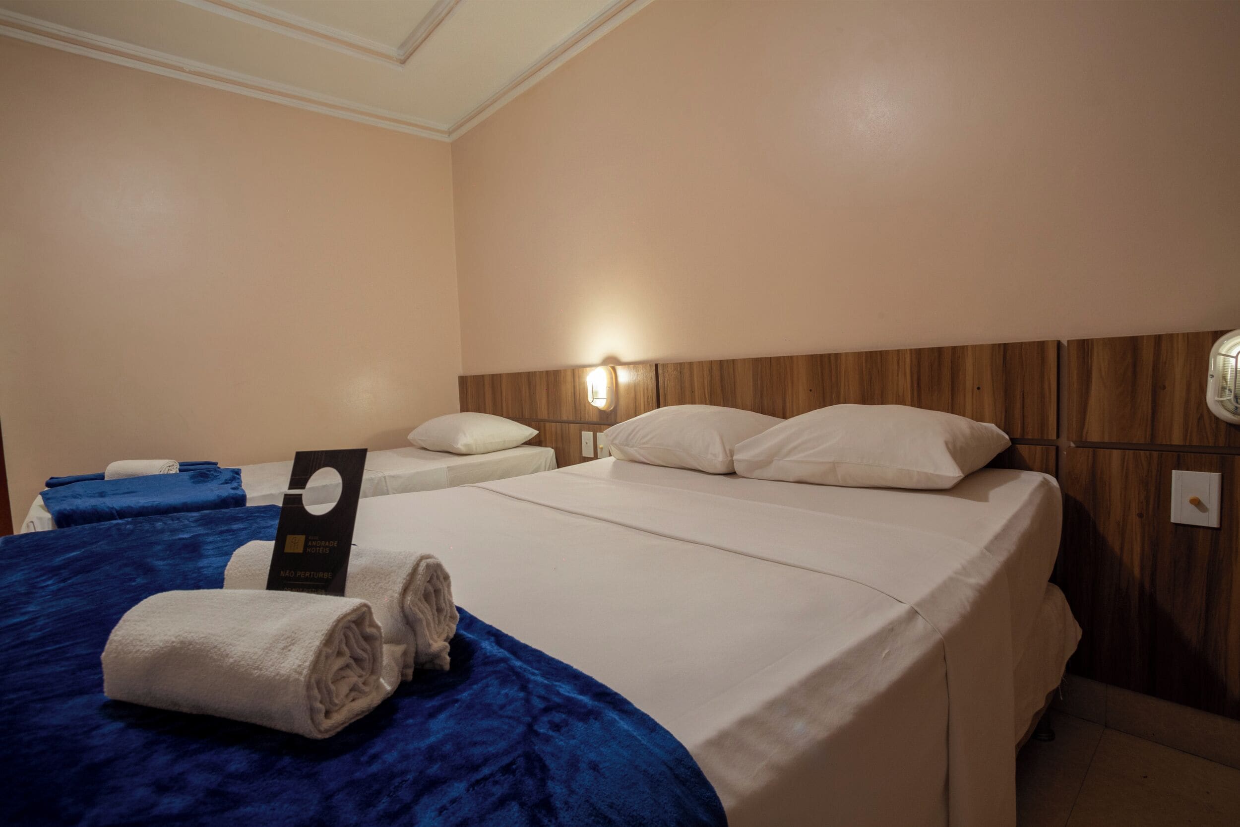 A hotel room with two beds, a wooden headboard, a wall-mounted light, and a sign indicating the room type.