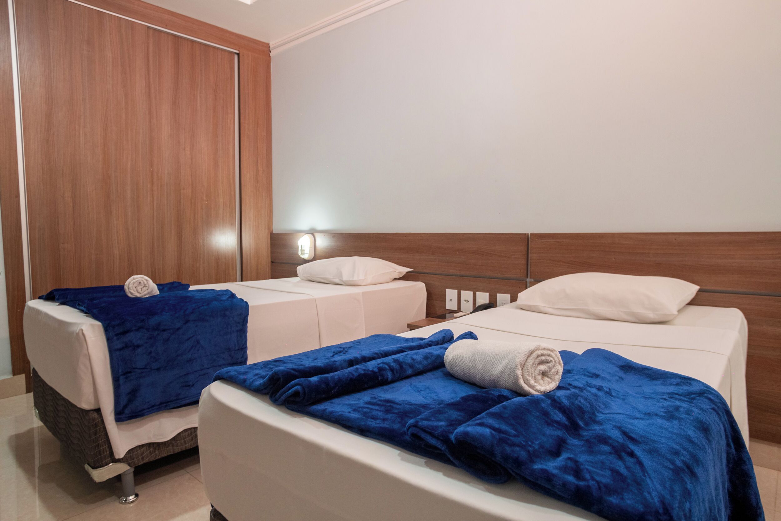 Een hotelkamer met twee bedden, elk met een blauwe deken en een wit kussen.